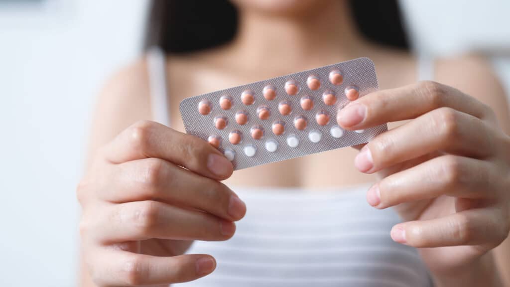 Young woman opening birth control pill package. 