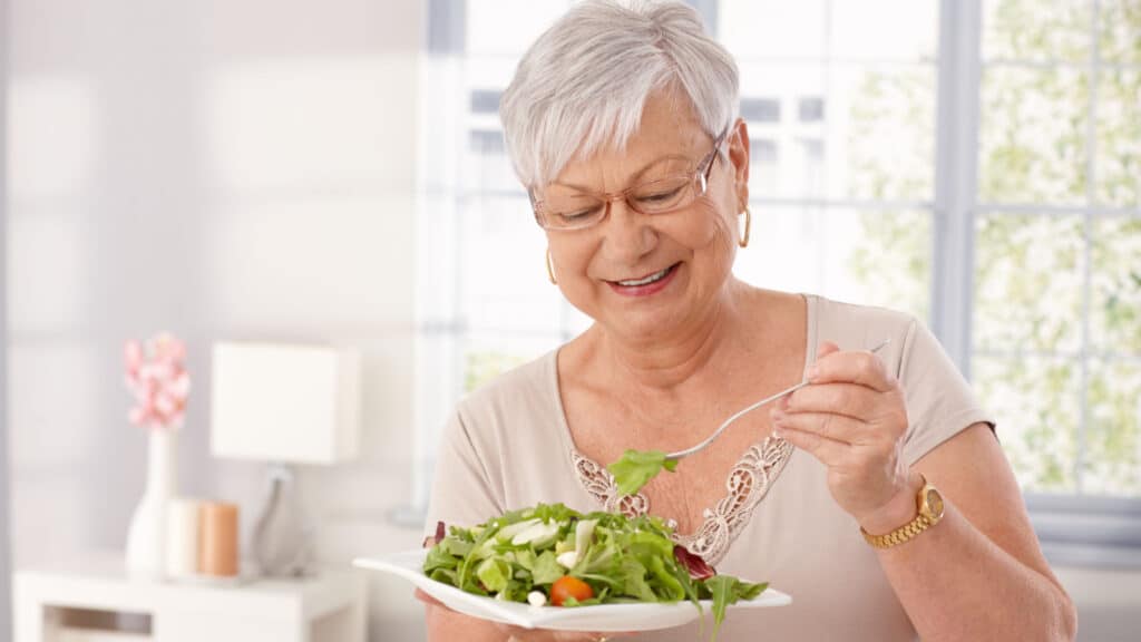 Happy older woman eating salad. 