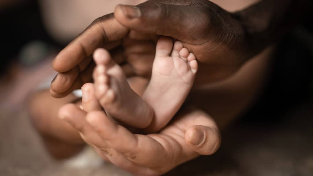 Interracial couple's hands holding baby's feet. 