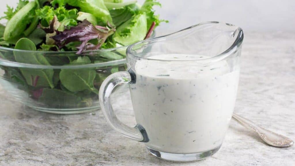 Low-FODMAP-Ranch-Dressing-in-clear-glass-pitcher-green-salad-in-background.