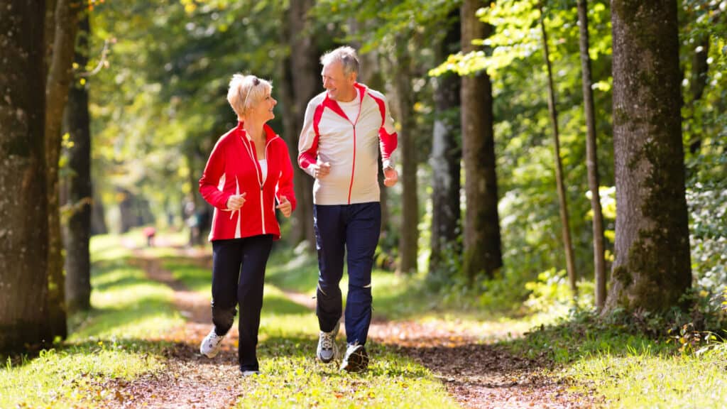 Older couple jogging running in woods. 