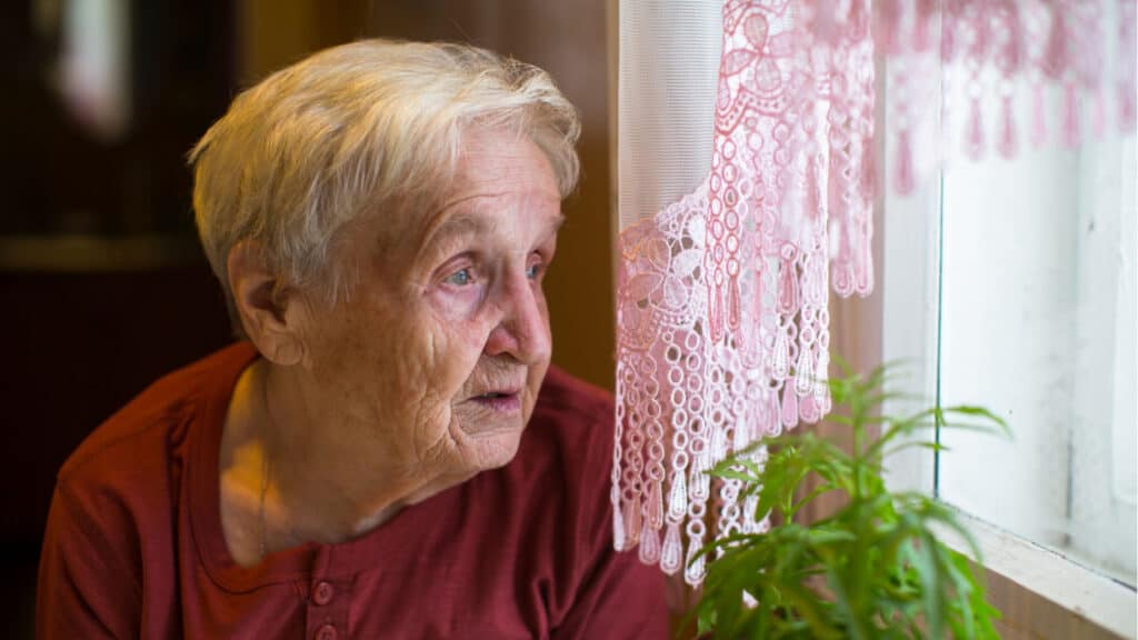 Older woman with longing looks out the window.