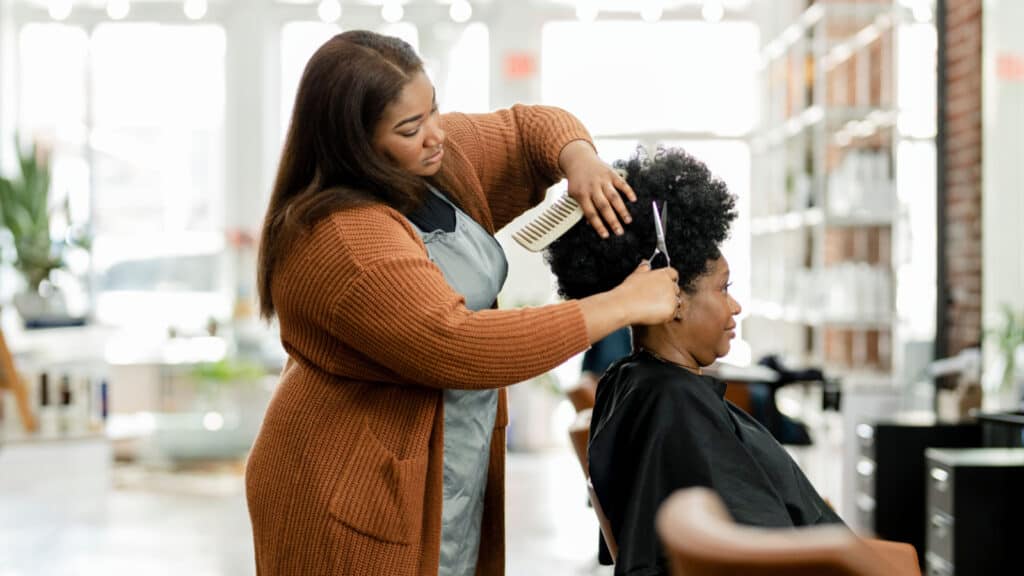 Hairstylist trimming the customer 39;s hair at a beauty salon black woman