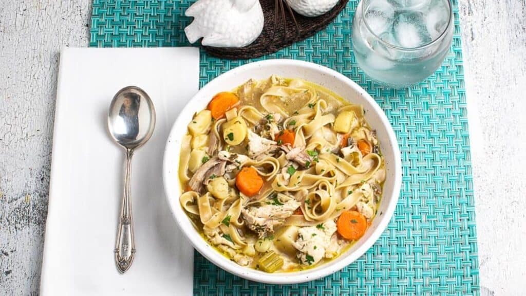 low-FODMAP-Instant-Pot-Chicken-Noodle-Soup-in-a-white-bowl-on-an-aqua-placemat-with-a-water-glass.