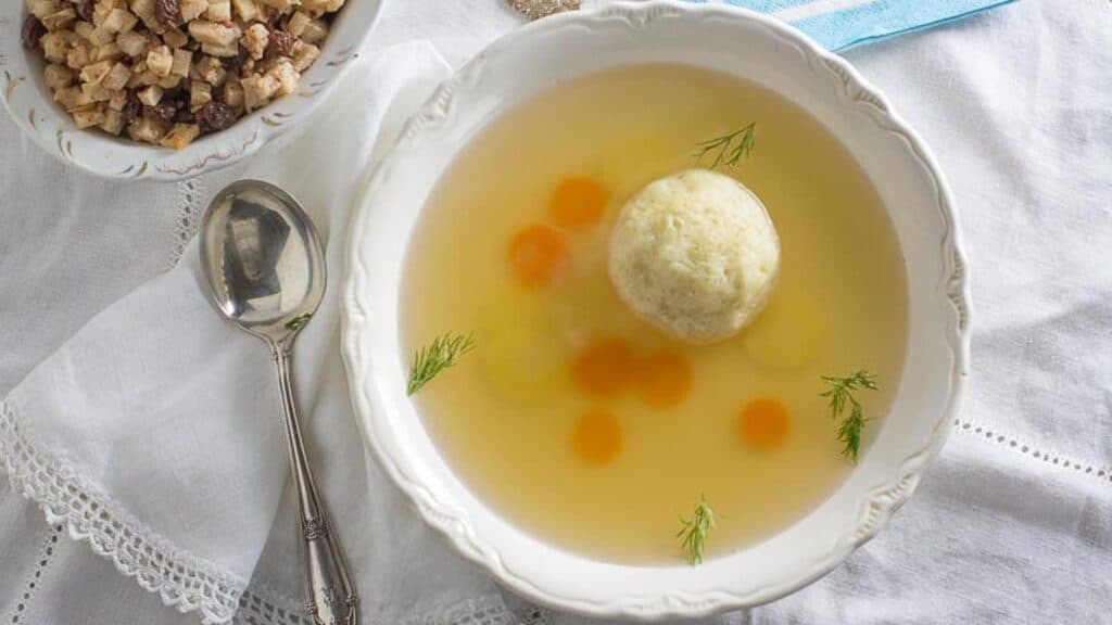 Matzo-ball-soup-in-a-white-bowl-with-charoset-in-the-background.