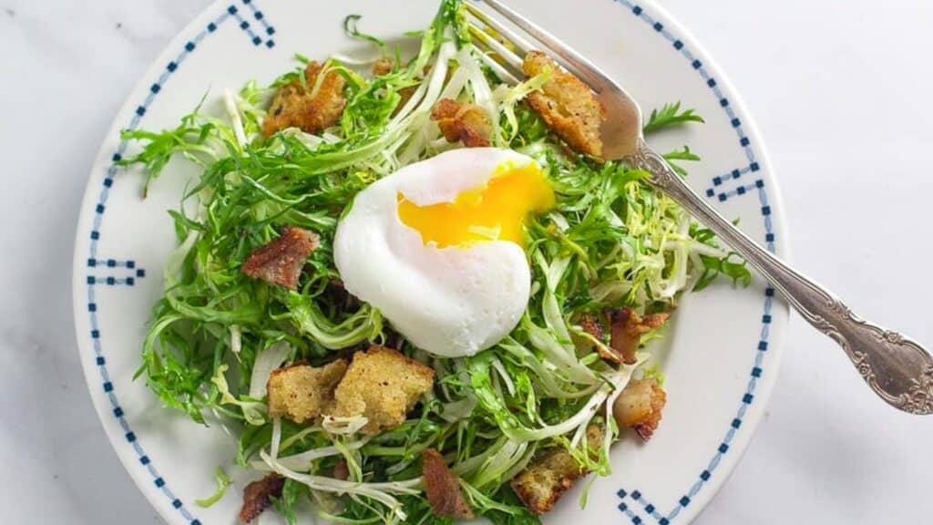 friseee-salad-with-poached-egg-broken-open-on-white-plate-with-blue-border.