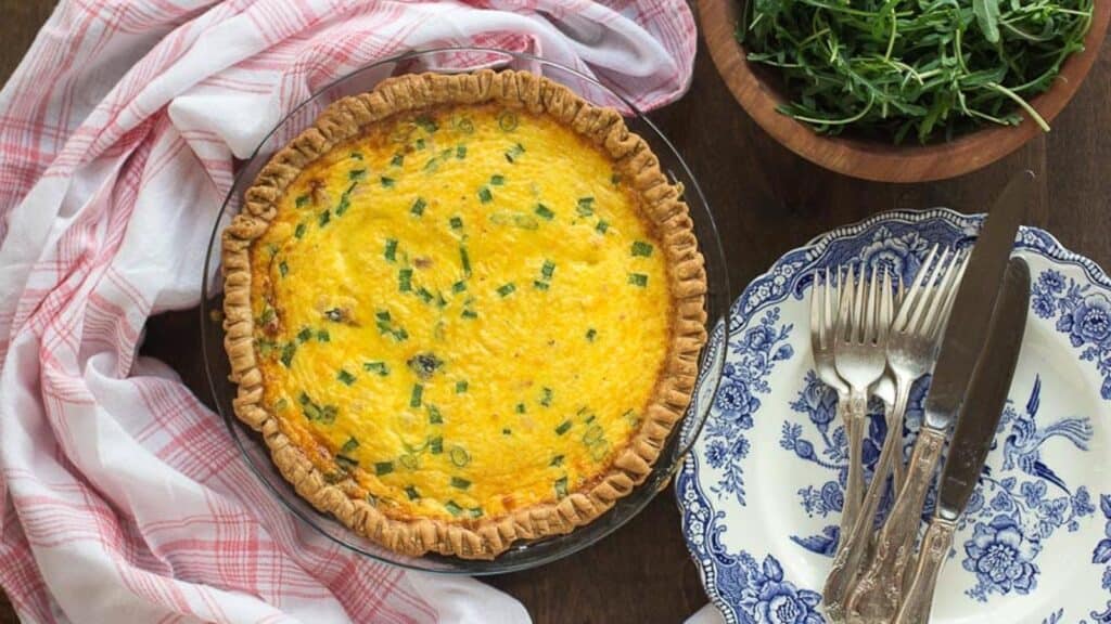 overhead-image-of-ham-cheese-low-FODMAP-quiche-whole-in-pie-pan-with-blue-and-white-plates-alongside.