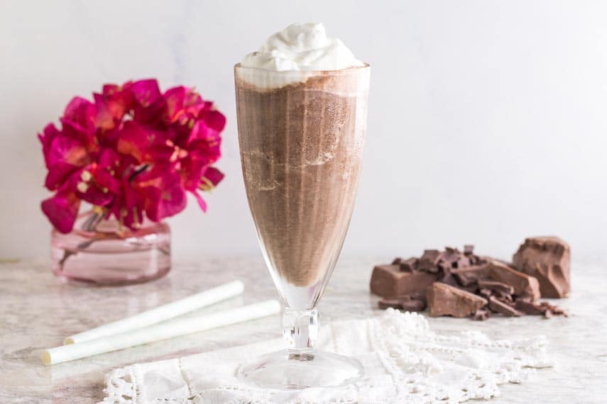 Frozen-Hot-Chocolate-in-glass-goblet-with-pink-flowers-straws-and-chopped-chocolate-in-background-on-white-surface-2.