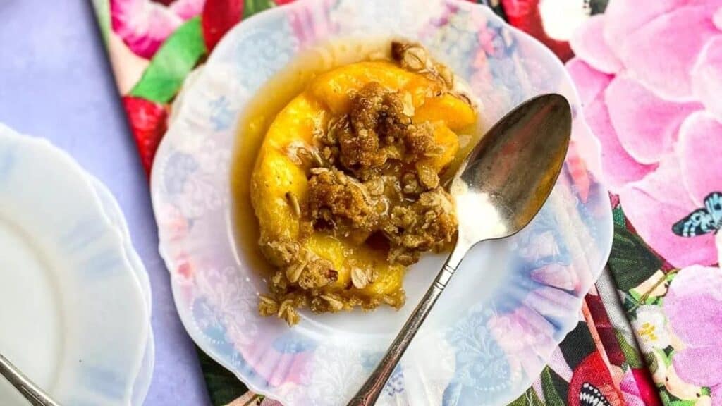 Close-Up-of-peach-crisp-on-white-plate-with-floral-napkins-and-silver-spoons.
