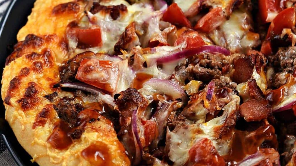 Close-up-image-of-a-sliced-bacon-cheeseburger-pizza-topped-with-cheese-beef-bacon-tomato-and-barbecue-sauce-on-a-blue-plate.-cookingwithcurls.com.