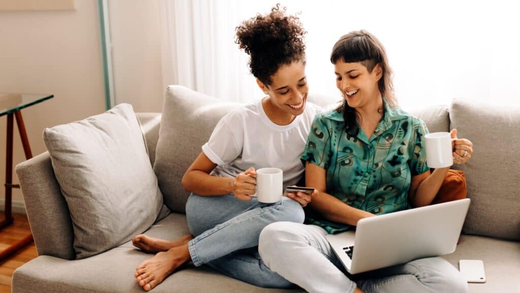 Lesbian couple drinking coffee and on laptop. 
