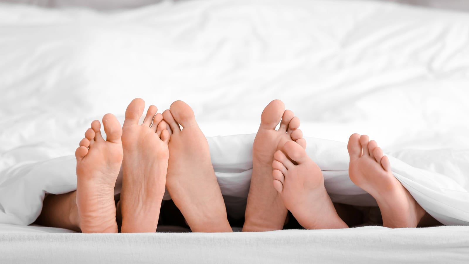 Feet of man and two women lying under blanket in bed. Polyamory concept
