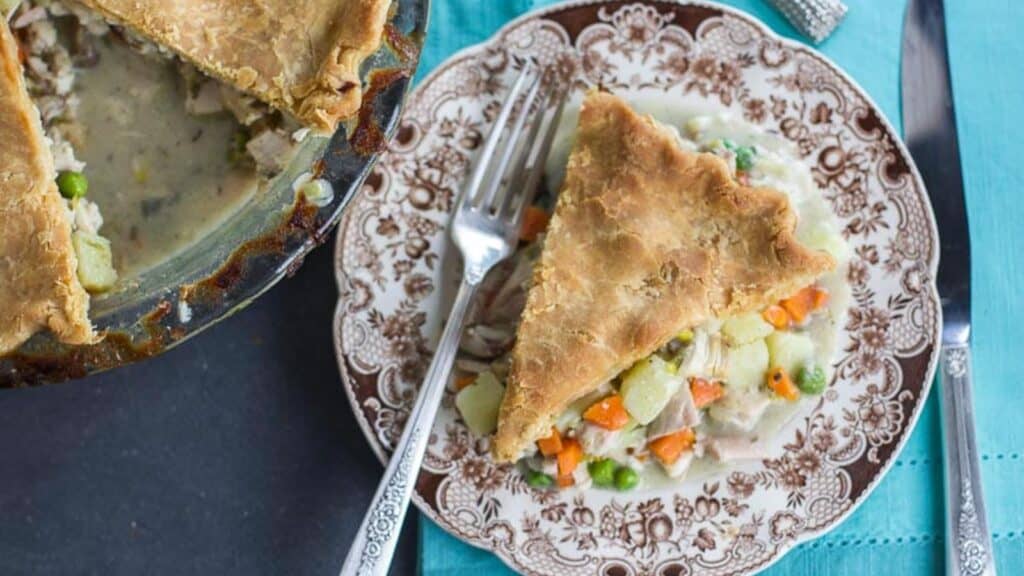 overhead-image-of-Low-FODMAP-CHicken-Pot-Pie-slice-on-brown-decorative-plate-on-teal-cloth-whole-pie-alongside.