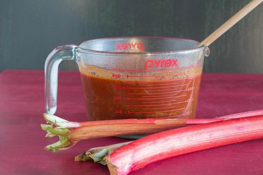 rhubarb-BBQ-sauce-on-measuring-cup-with-fresh-rhubarb-alongside.