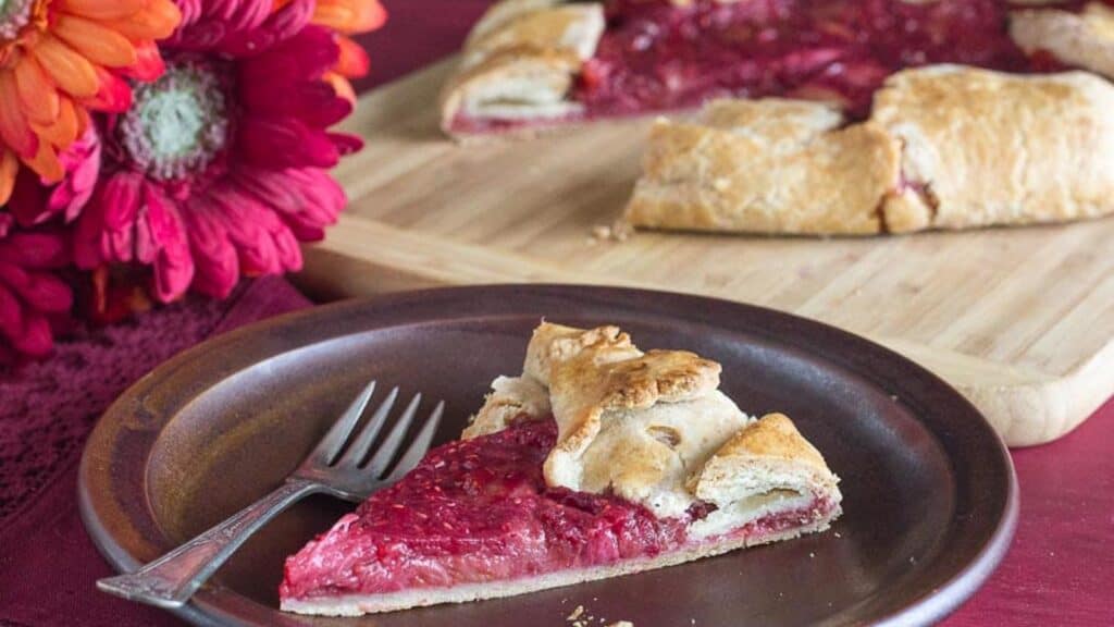 rhubarb-raspberry-crostata-slice-on-a-brown-plate-with-Gerbera-daisies-in-background.