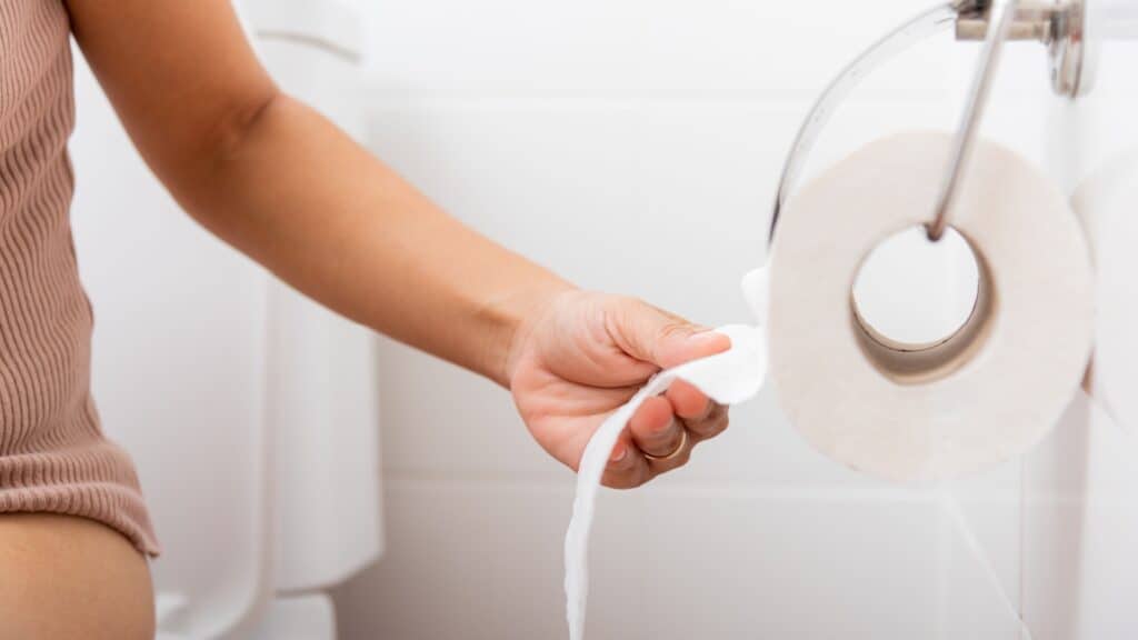 woman pulling on toilet paper roll. Bathroom.